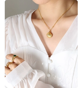 Close-up of gold scallop pendant necklace and emerald green gemstone ring on a model