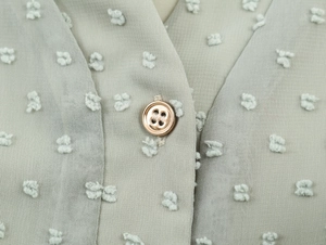 Détail du bouton rond sur robe en mousseline vert clair avec pois texturés en relief