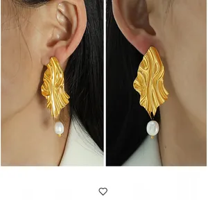 Detailed view of exaggerated gold irregular wavy metal earrings with pearl charms