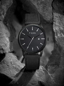 Detail of minimalist black matte watch dial with date window set against grey rock