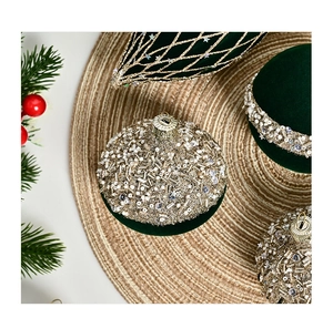 Close-up of green flocked Christmas ornaments with gold sequins and pearls on pine branches