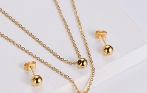 Detailed view of polished gold sphere necklace and stud earrings set on a white stand