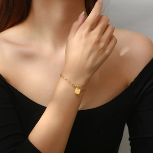 Close-up of a delicate gold chain bracelet with a minimalist square pendant on a wrist