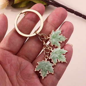 Close-up of golden keychain with three green enamel maple leaf pendants held in hand