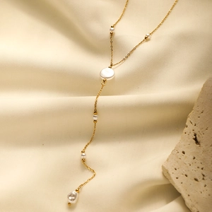 Detail of gold-plated pearl tassel necklace displayed on beige velvet and stone