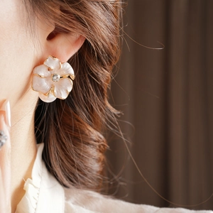Détail d'une boucle d'oreille fleur vintage aux pétales blancs, bord doré et cristal central