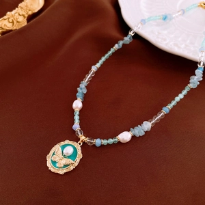 Close-up of aquamarine beads and pearl necklace with a vintage gold butterfly pendant