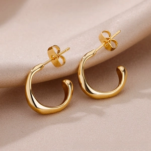 Macro detail of gold triple-layer C-shaped hoop earrings on elegant silk background