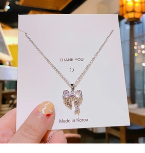 Détail d'un collier nœud en argent avec pendentif zircon sur une carte de remerciement