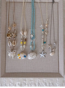 Detail view of five ocean-themed necklaces with seashells and starfish on a display