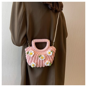 Detail of pink woven handbag with white daisy decor and pearl strap worn by a model