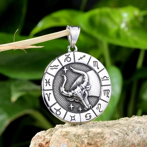 Macro shot of a silver Taurus zodiac pendant resting on a textured rock with nature background