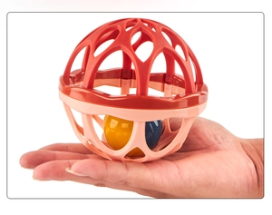 Close-up of baby grasping ball toy showing the red and pink hollow grid and inner rattles