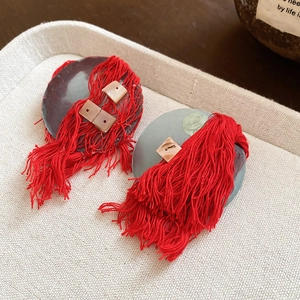 Macro shot of silver needle shell earrings with red silk tassels on a beige fabric tray