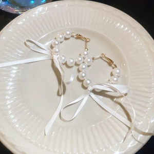 Macro view of French style pearl hoop earrings with white silk bows on a plate