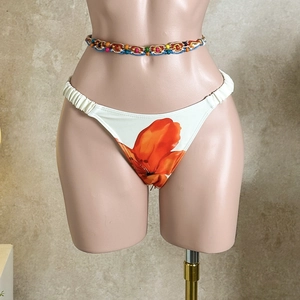 Detail of white bikini bottoms with orange floral print and ethnic woven bead waist belt