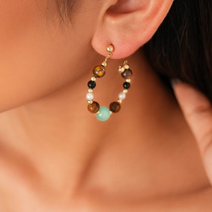 Close-up of vintage hoop earring with tiger eye, pearls and stones on a model