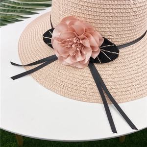 Detail of hand-woven straw hat featuring a large beige fabric flower and black ribbons