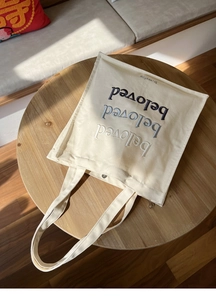 Detail of embroidered beloved text in three colors on off-white canvas tote bag