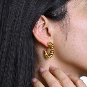 Close-up of a woman wearing gold twisted spiral C-hoop earrings with textured finish