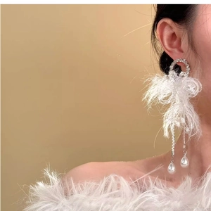Detailed shot of bow-shaped fringe earrings with white feathers and pearl charms