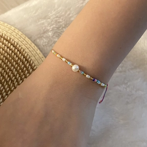 Close-up of woven colorful seed bead bracelet with central pearl on a person's wrist