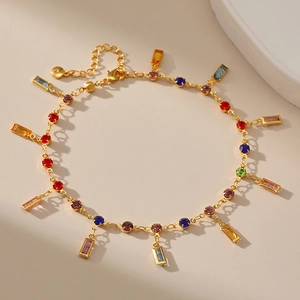 Golden chain anklet with colorful round and rectangular crystal pendants on beige background