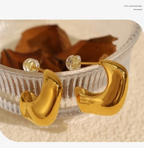Macro shot of gold geometric C-shaped earrings with a smooth polished finish on a glass bowl