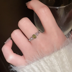 Detail view of oval olive green gemstone ring with silver hollow woven band on hand
