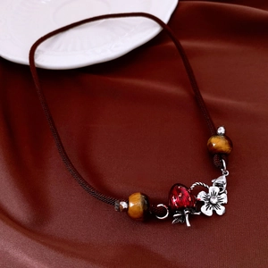 Macro detail of tiger eye beads and red strawberry flower pendant on brown cord