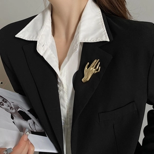 Detailed view of a polished gold palm-shaped brooch pinned on a black suit lapel