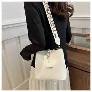 Close-up of white bucket bag featuring lychee grain leather and wide lettered shoulder strap