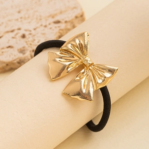 Detail of a minimalist gold metal bow hair tie on a beige textured cylindrical stand