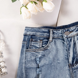 Dettaglio di pantaloncini in denim a vita alta con bottone metallico e strappi decorativi