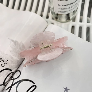 Pinza per capelli in resina rosa marmorizzata con strass argentati su una rivista bianca