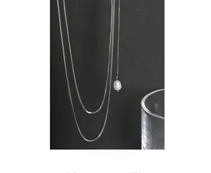 Macro shot of silver snake chain necklace with elegant white pearl pendant on black background