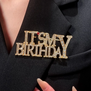 Detail of gold IT'S MY BIRTHDAY letter brooch with colorful rhinestones on black suit