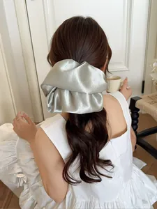 Close-up of a oversized silver-gray satin scrunchie worn on a high bun hairstyle