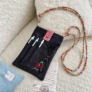 Detail of denim crossbody bag with cherry embroidery and colorful beaded strap