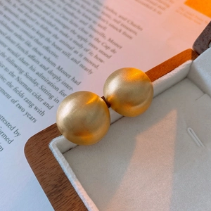 Macro shot of minimalist gold plated matte round ball stud earrings on a vintage prop