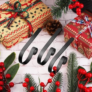 Close-up of three black metal Christmas stocking hooks on a festive brick mantel