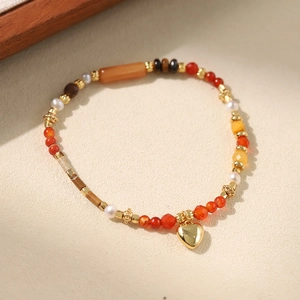 Macro shot of colorful beaded bracelet featuring a polished gold heart charm and pearls