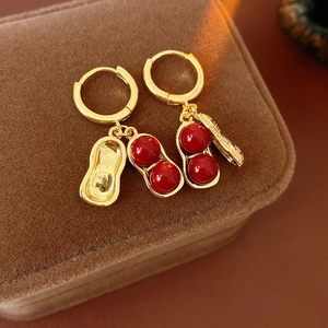 Close-up of gold peanut-shaped earrings with red glass beads on a brown velvet background