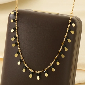 Detail of golden tassel necklace featuring faceted black beads and teardrop pendants