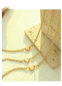 Three gold Cuban link necklaces with heart pendants on natural stone in warm sunlight