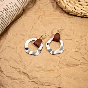 Detail of silver wavy earrings with brown leather accents on a textured backdrop