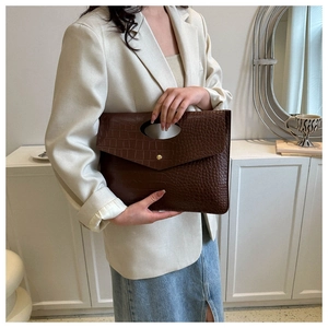 Detail of dark brown crocodile pattern envelope bag with gold buckle on white blazer