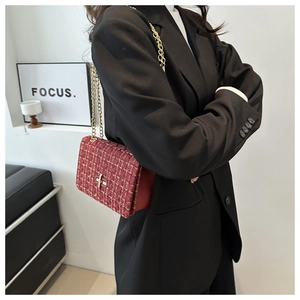 Detail of burgundy tweed chain bag with gold hardware worn over a black blazer
