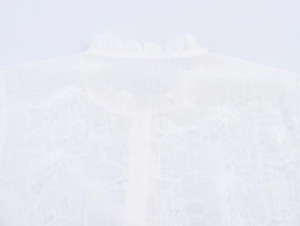 Detail of white blouse featuring ruffled collar and textured breathable fabric texture