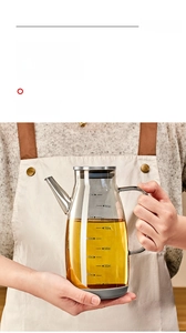 Close-up of hand holding a glass oil dispenser with clear scale marks and C-shaped handle